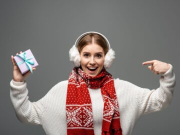a woman wearing earmuffs, a sweater and a scarf holding a gift