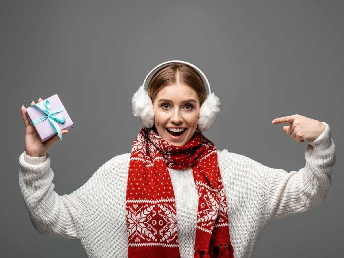 a woman wearing earmuffs, a sweater and a scarf holding a gift