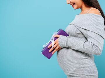 a pregnant woman holding a purple gift by her belly bump