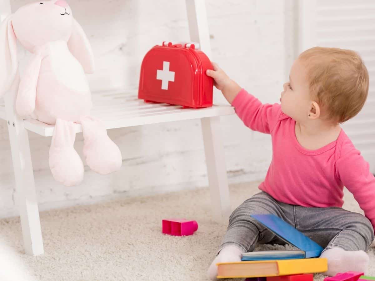 a baby holding a pretend play first aid kit.