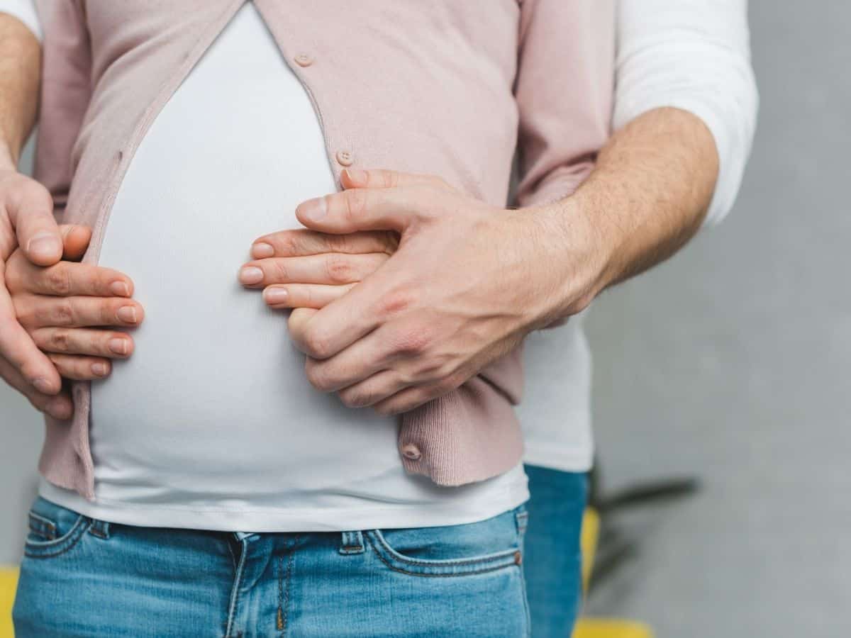 a pregnant woman with her husband's arms around her