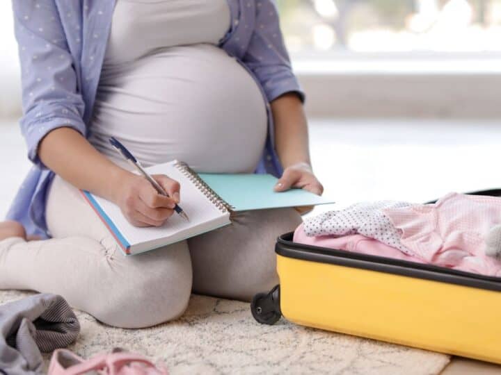 a pregnant woman making a checklist next to her yellow suitcase