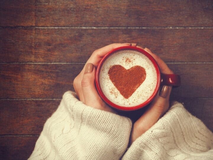 a pair of hands holding a red coffee mug with a heart in the coffee froth