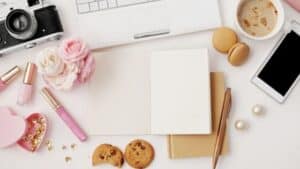a computer flatlay with a camera, phone and notebook