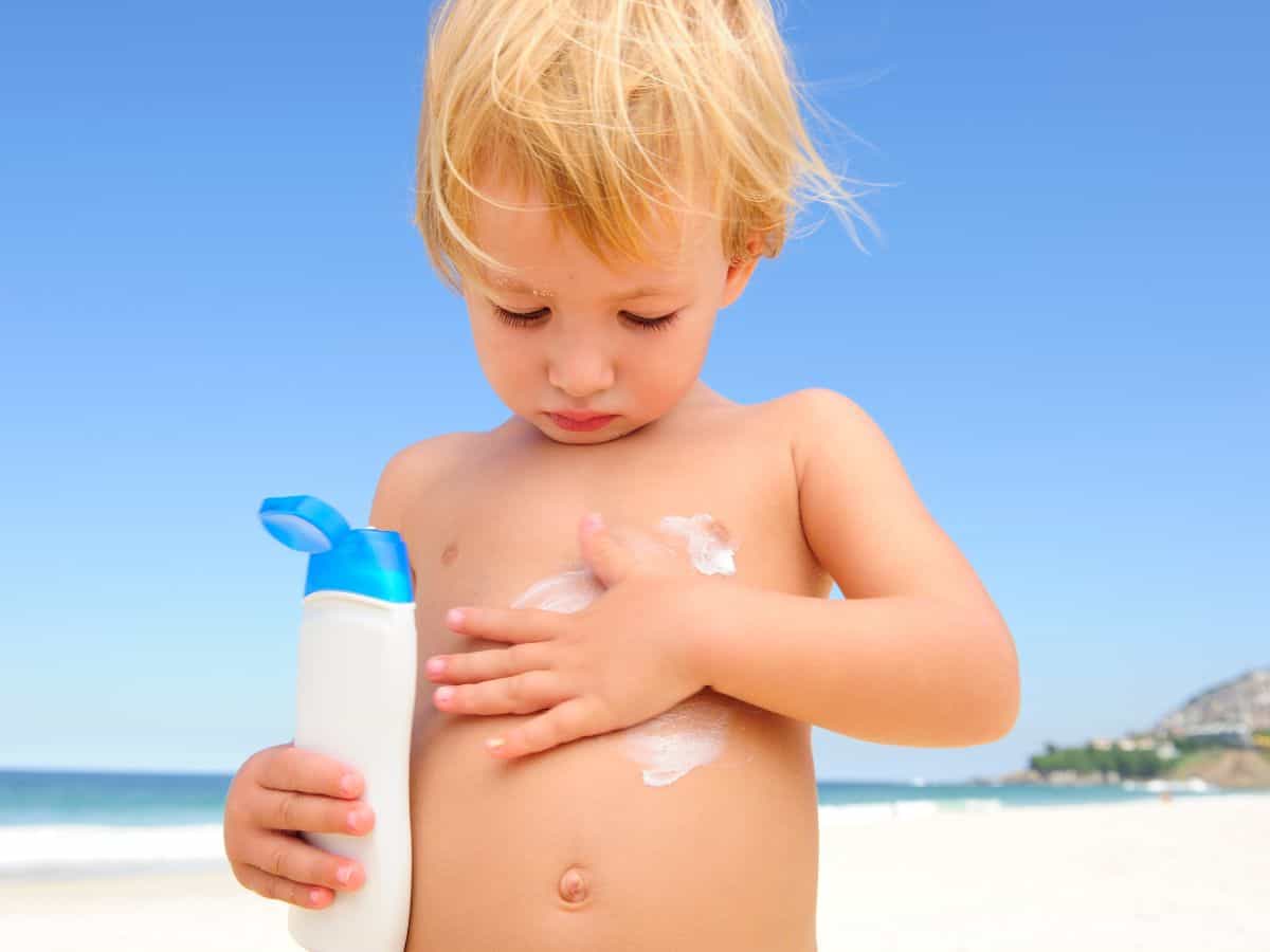 a little boy putting sunscreen on at the beach