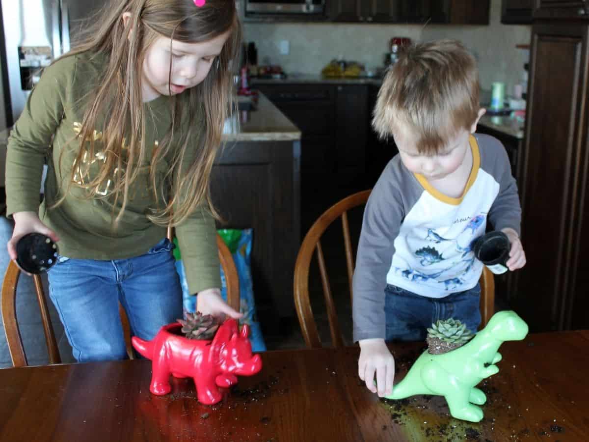 two kids putting succulents into dinosaur planters