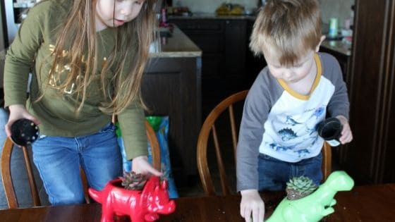 two kids putting succulents into dinosaur planters