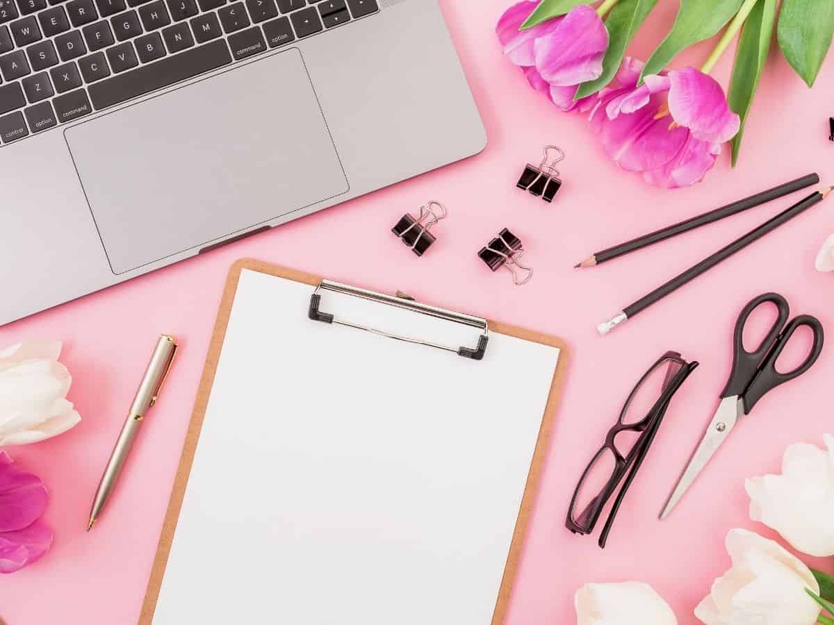 an overhead view of a pink desk with a computer clipboard and other office supplies