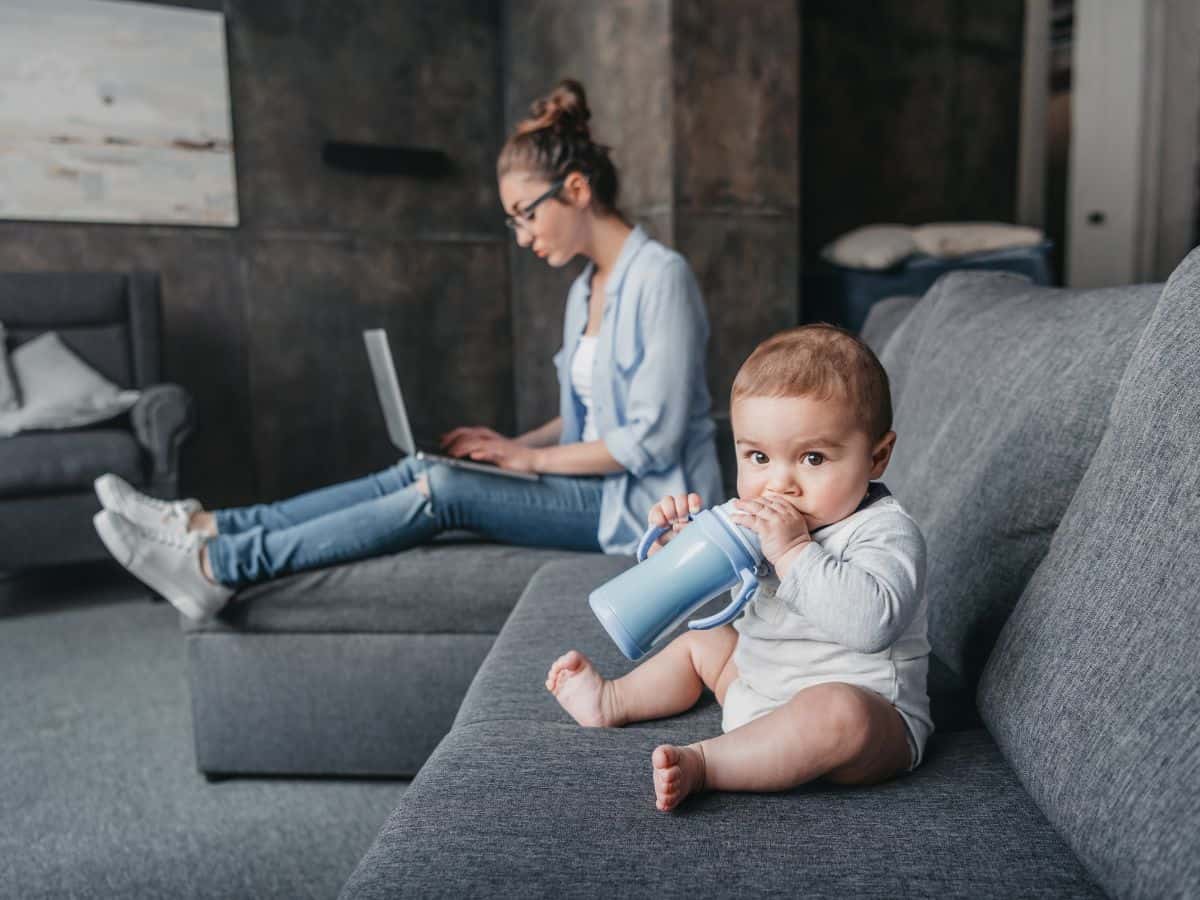 a mom sitting on the couch with her laptop and her baby nearby her