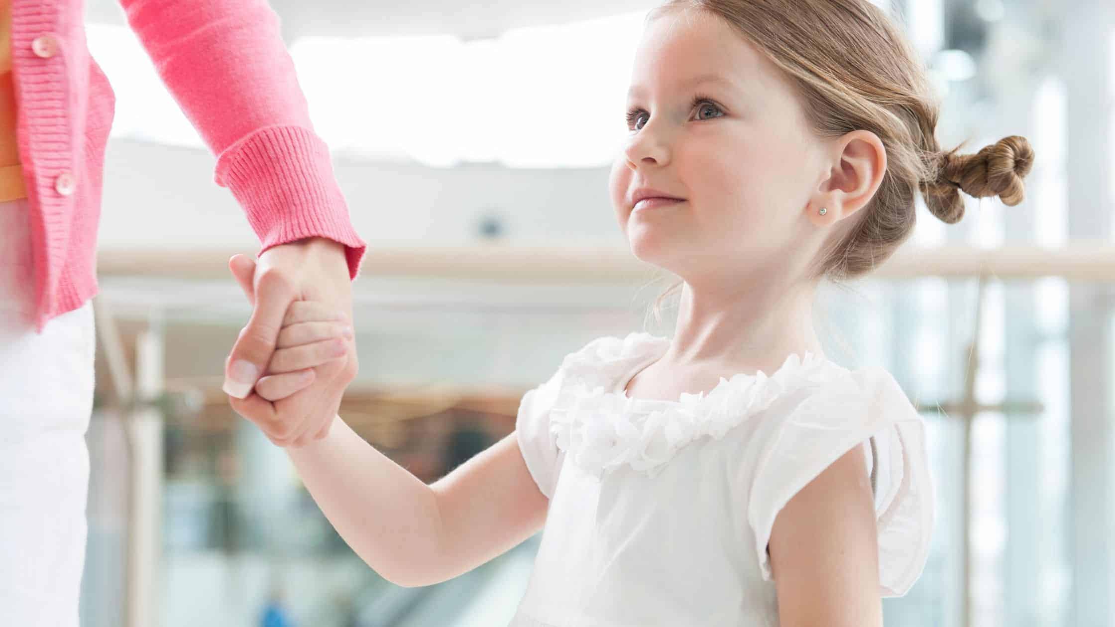 a mom holding her daughter's hand while they are out in public