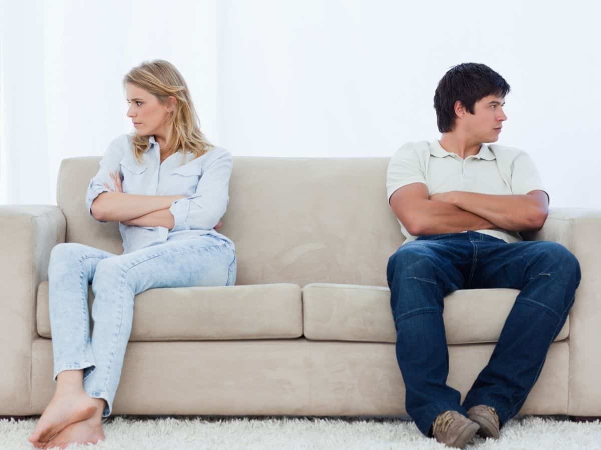 a married couple who are upset and looking in different directions while sitting on the same couch.