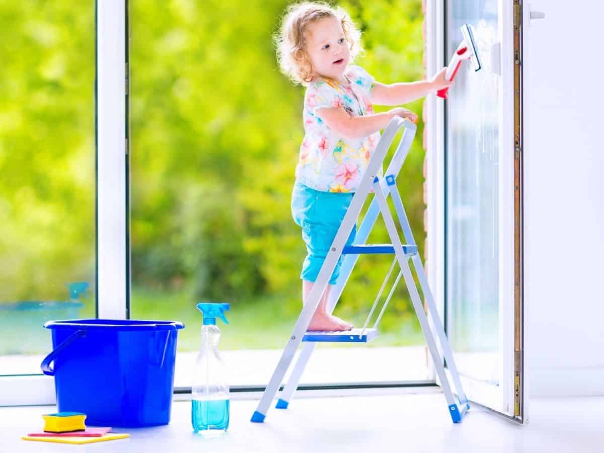 a toddler girl on a step ladder wiping windows