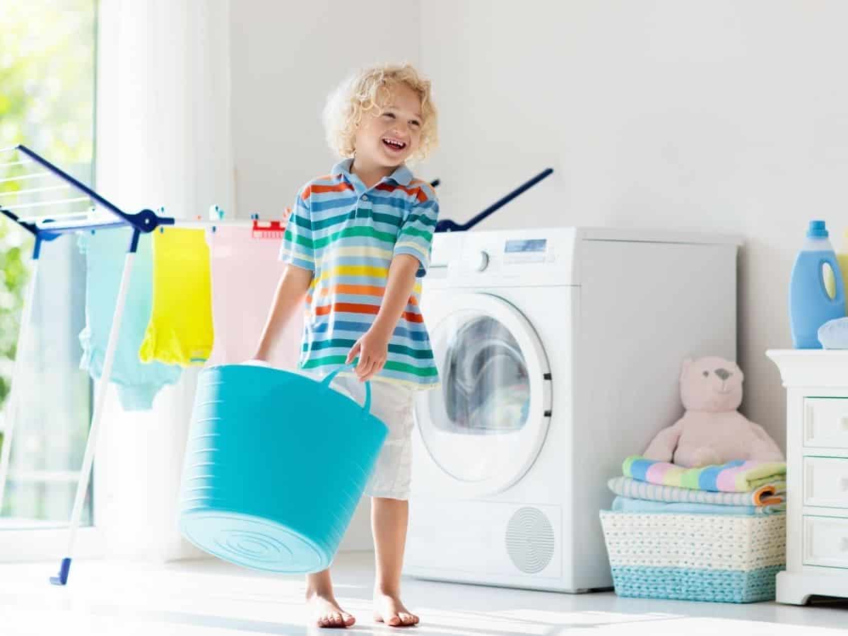 a young boy bring laundry into the laundry room