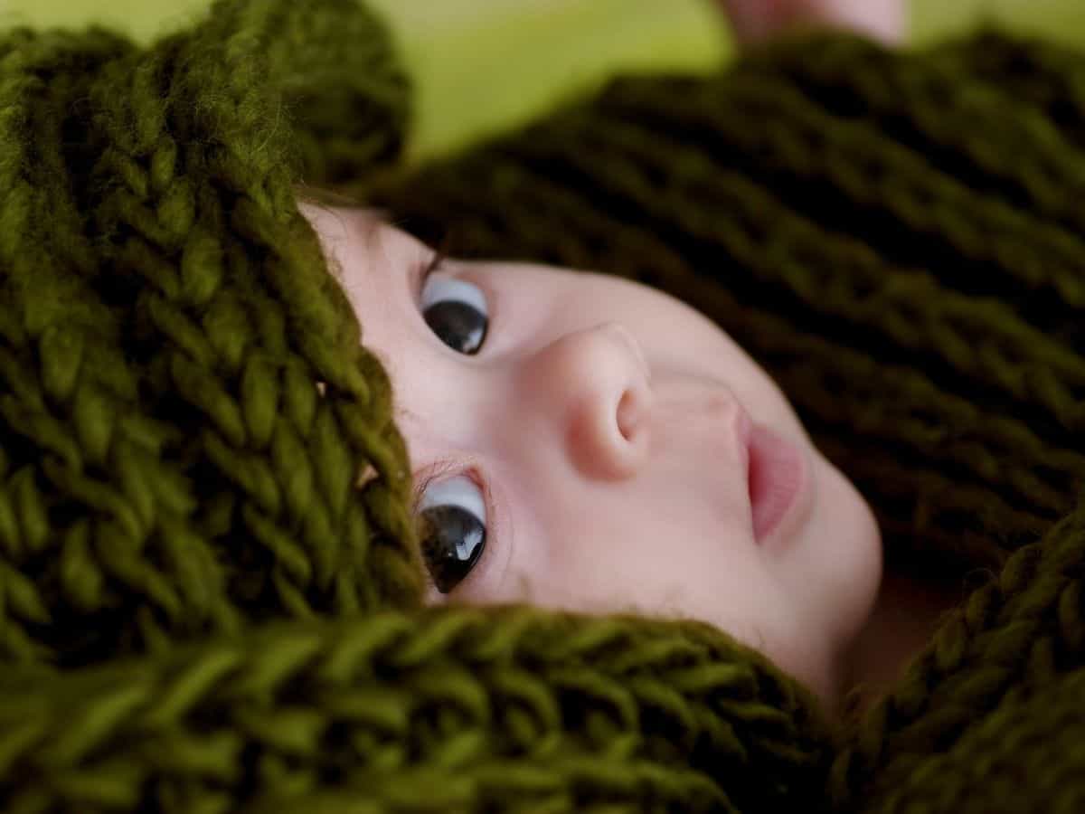 a baby wrapped in a dark green crochet blanket