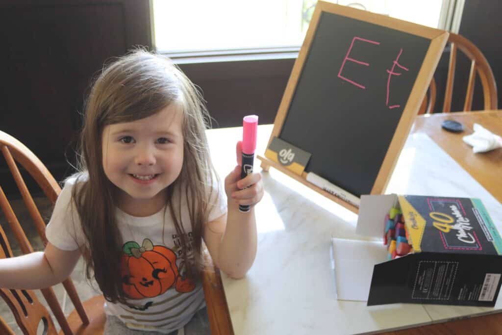 a girl holding a chalk marker next to a little chalkboard