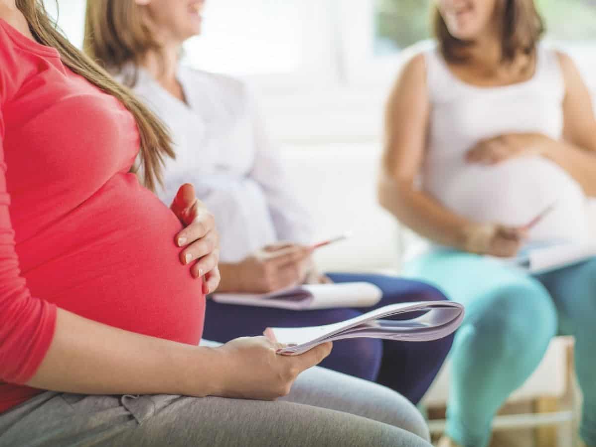 a pregnant woman holding her baby bump and two other pregnant women in the background