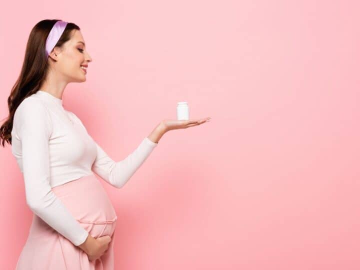 a pregnant woman holding a bottle of prenatal vitamins