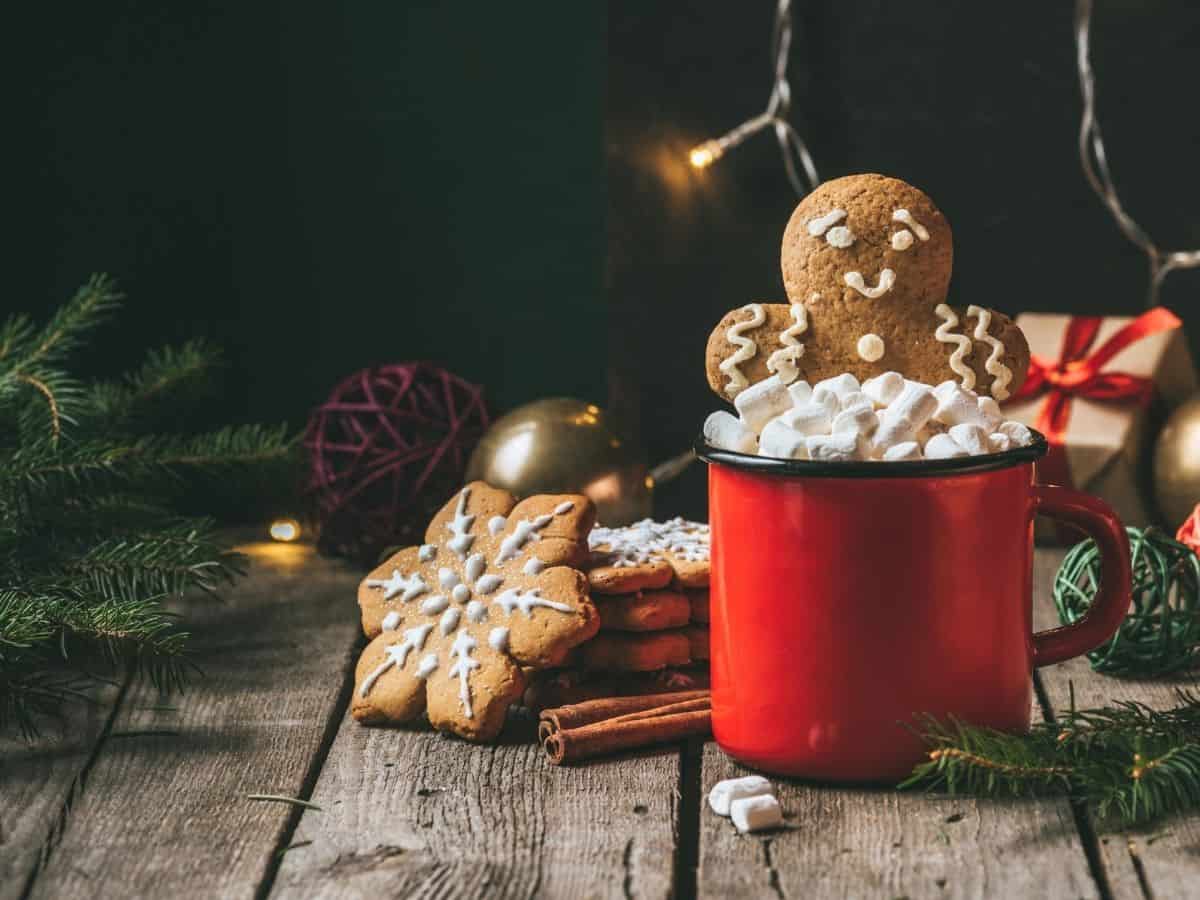 a gingerbread man cookie in a mug of cocoa and other decorated cookies nearby