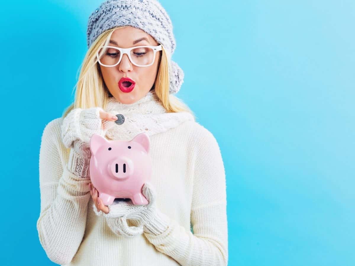 a woman dressed in winter clothes putting coins in a piggy bank.