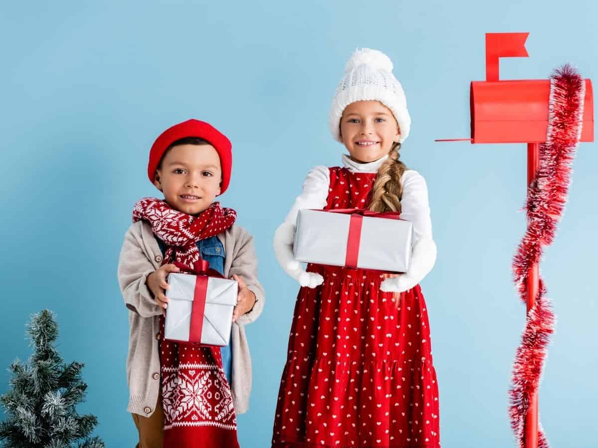 a boy and girl holding gifts near a christmas tree and a mailbox