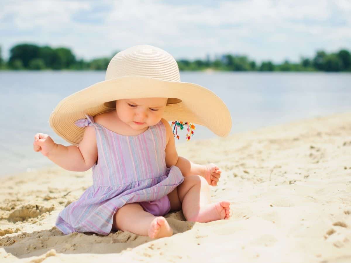 a little baby girl at the beach wearing a large sun hat