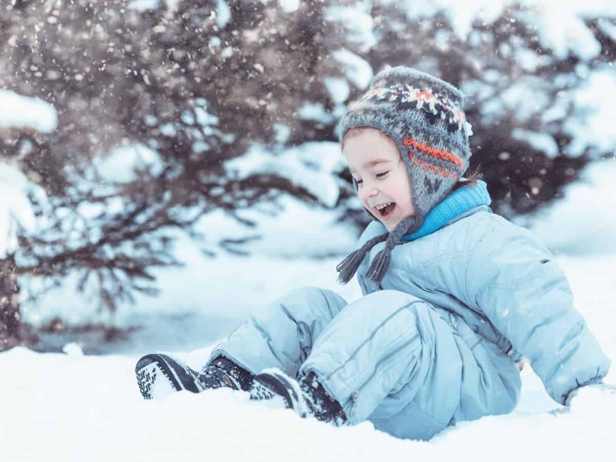 a toddler playing in the snow wearing warm winter clothes and snow boots