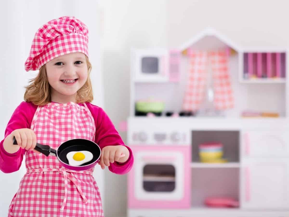 a little girl with a pretend chef outfit cooking at her pretend kitchen