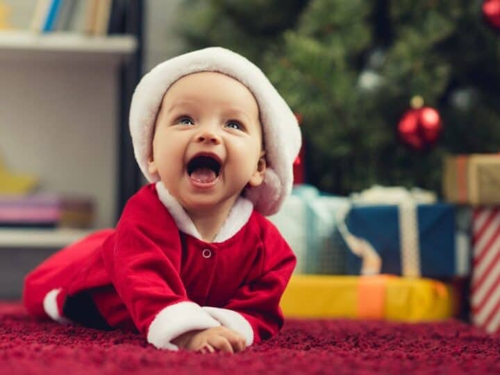a smiling baby in a santa costume and a christmas tree in the background