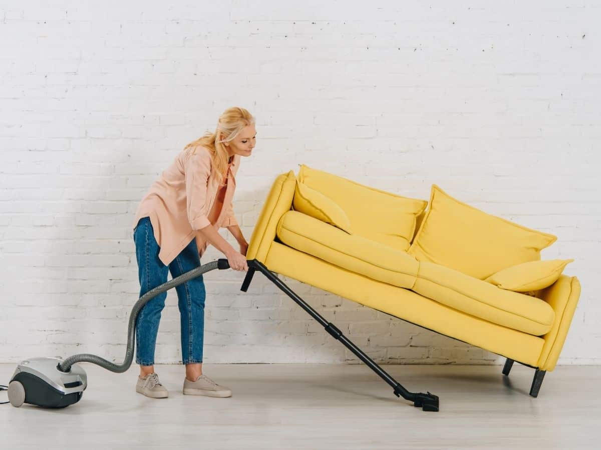 a mom lifting a couch up to vacuum under