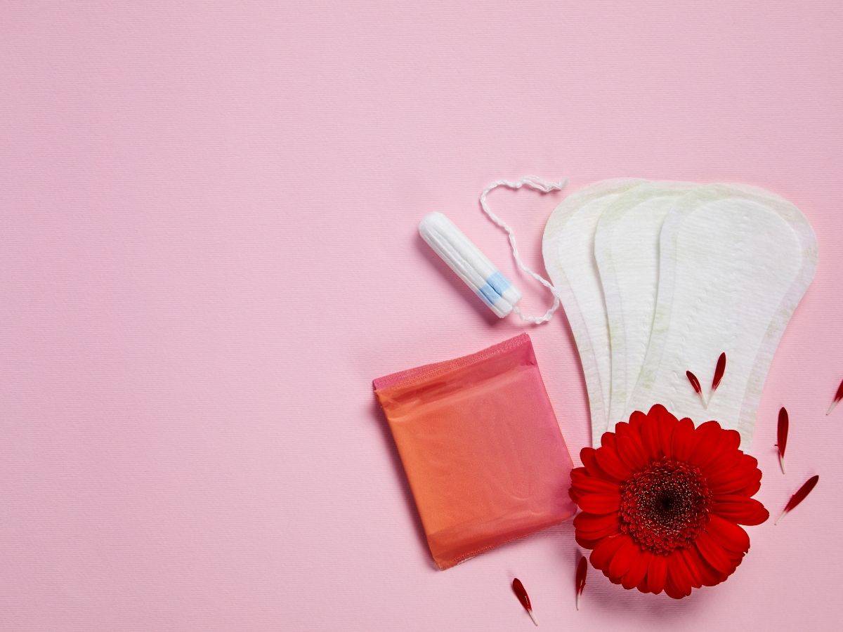 a bunch of period products on a pink background including some pads, and a tampon