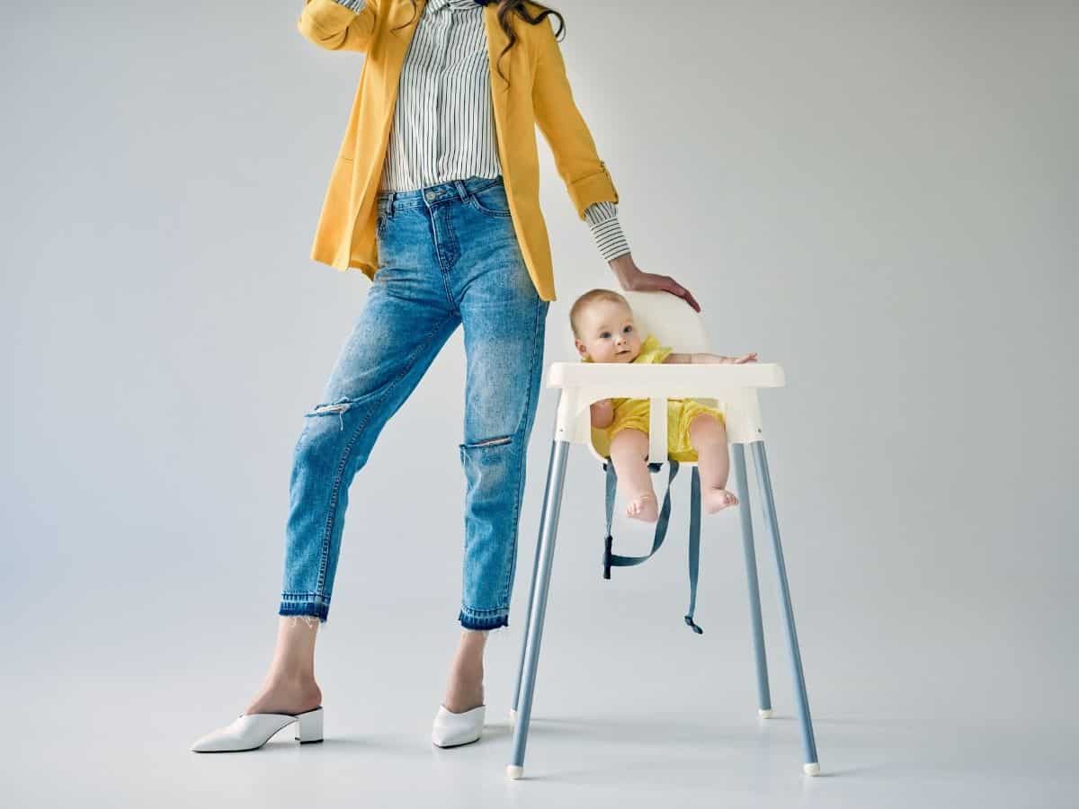 a mom standing by her baby who is in a high chair.