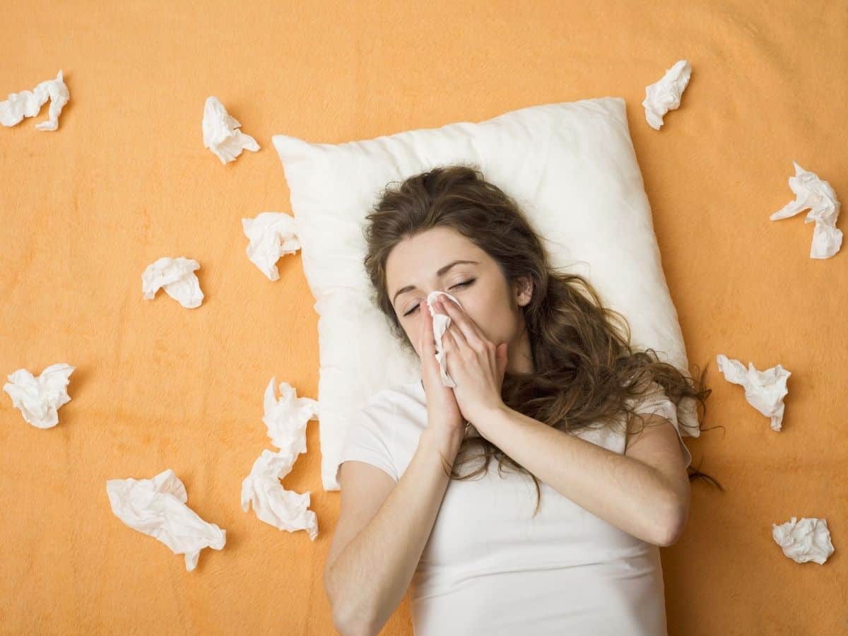 a woman blowing her nose, surrounded by tissues