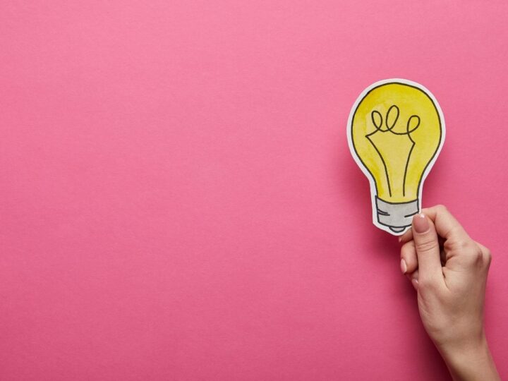 a hand holding up an image of a lightbulb on a pink background