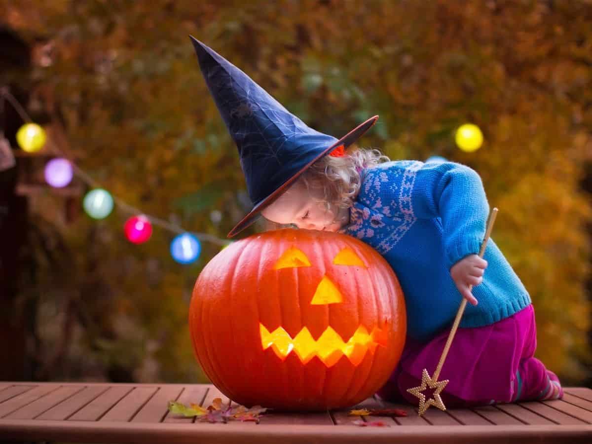 a little girl wearing a witch hat and looking at a jack-o-lantern pumpkin