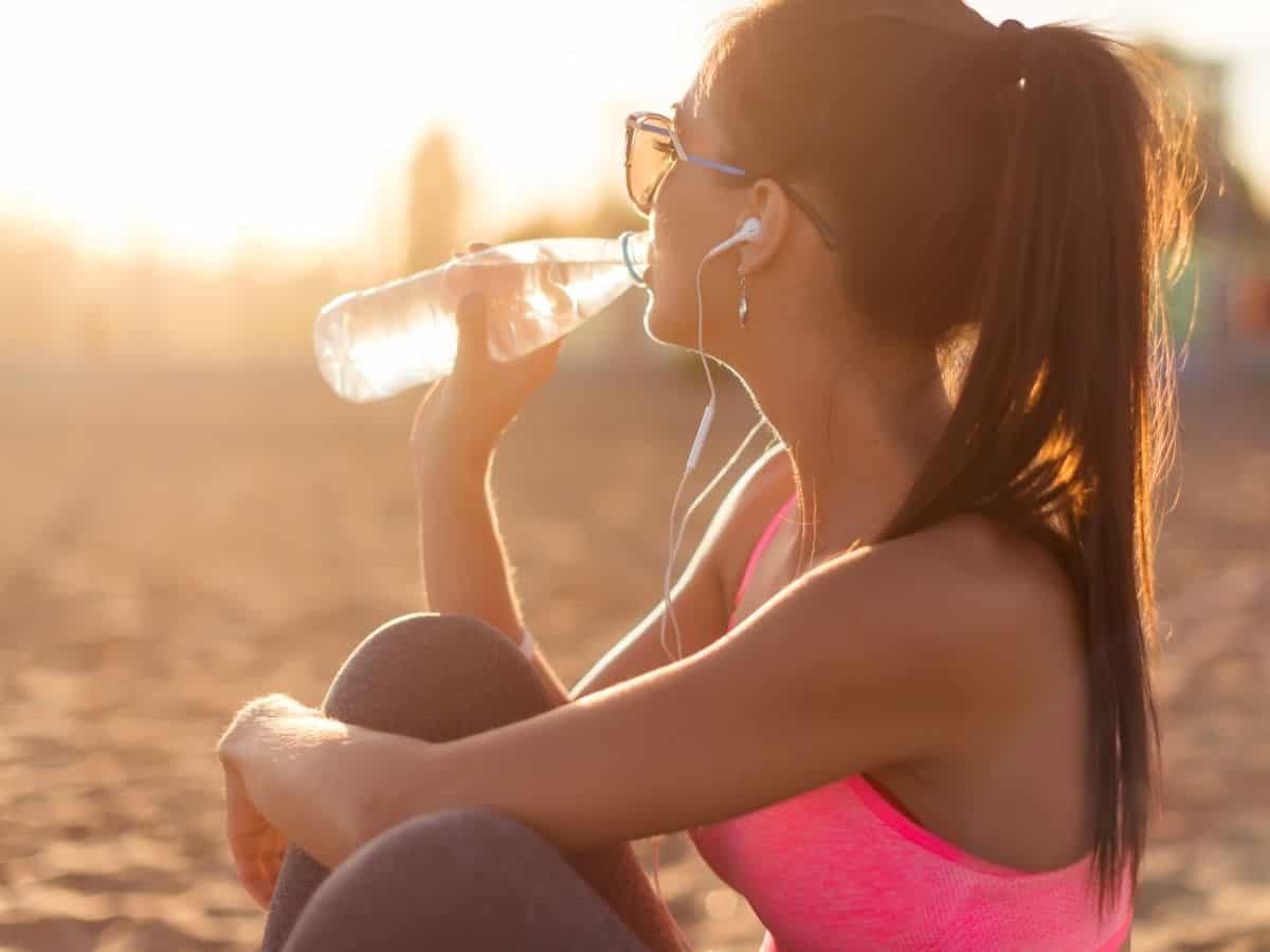 a woman drinking water outside while wearing athletic clothes