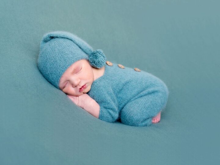 a newborn in a blue onesie and hat on a blue blanket