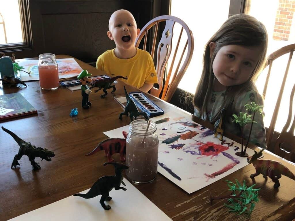 kids painting with toy dinosaurs nearby