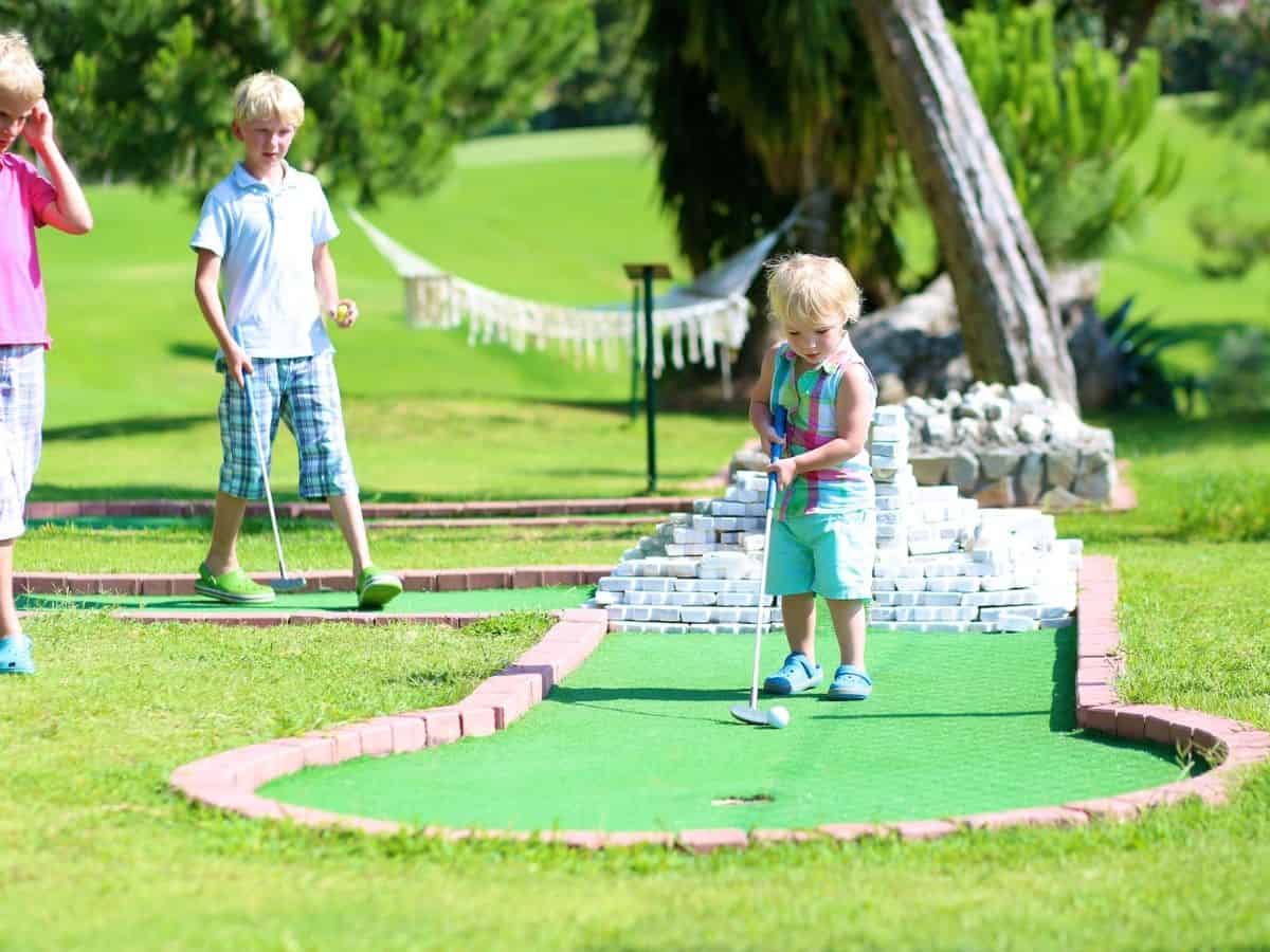 three kids playing mini golf outside