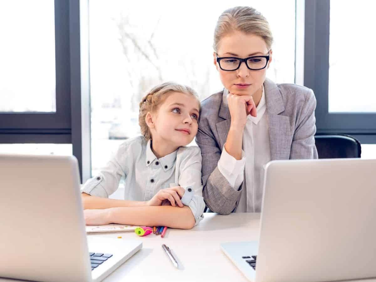 a mom and daughter sitting beside each other at a desk with two laptops