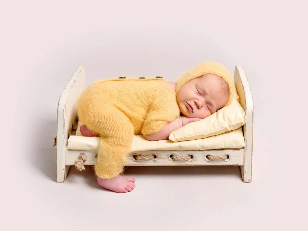 a baby boy in a yellow outfit sleeping of a miniature bed