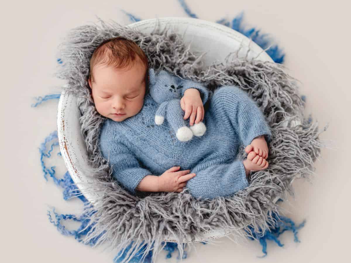 a baby boy in a blue outfit sleeping in a basket