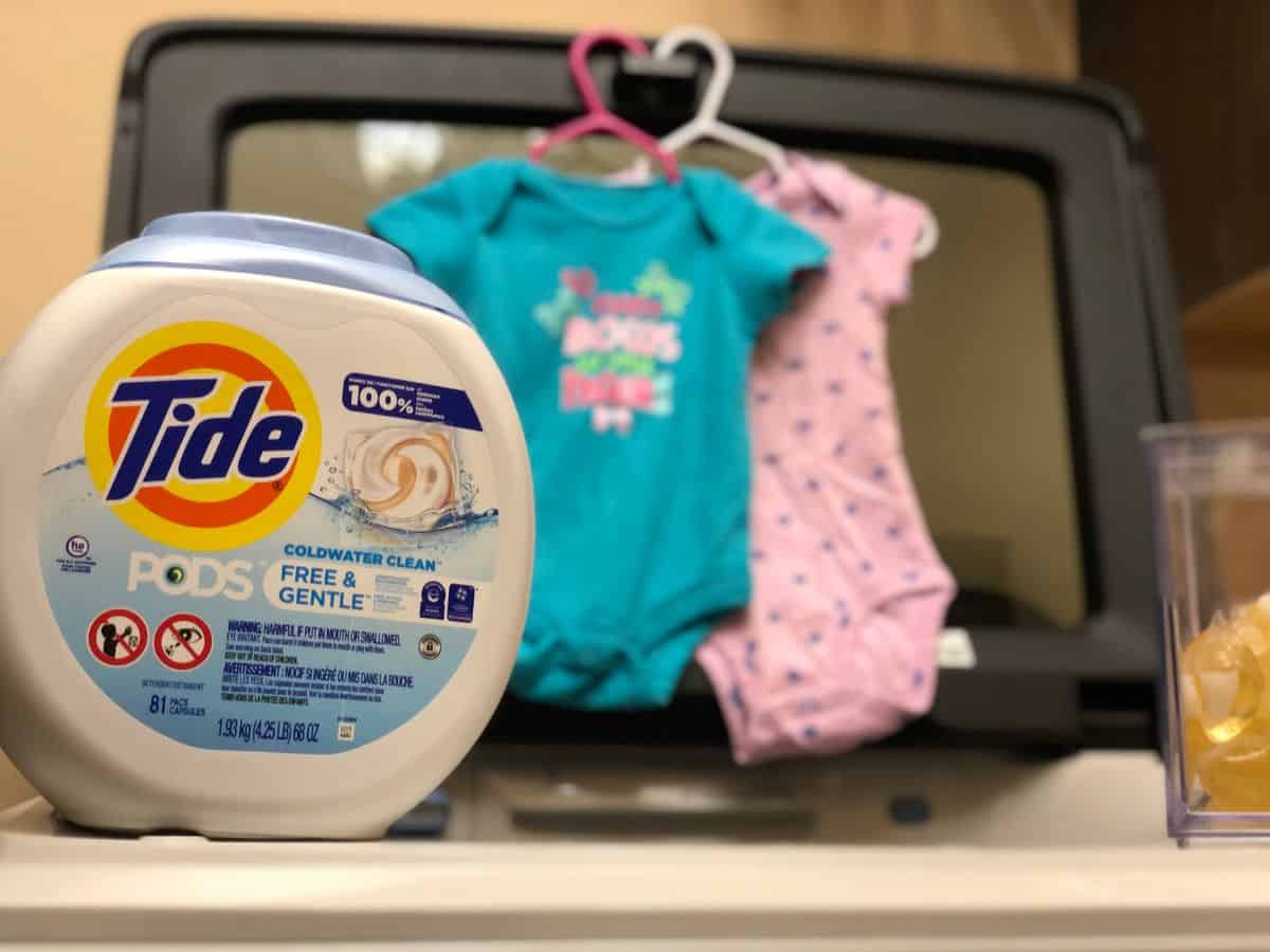 a laundry detergent on a washer with to baby onesies nearby