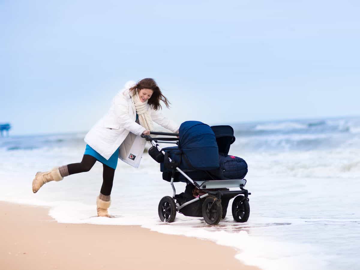 a mom pushing a side by side double stroller on the beach