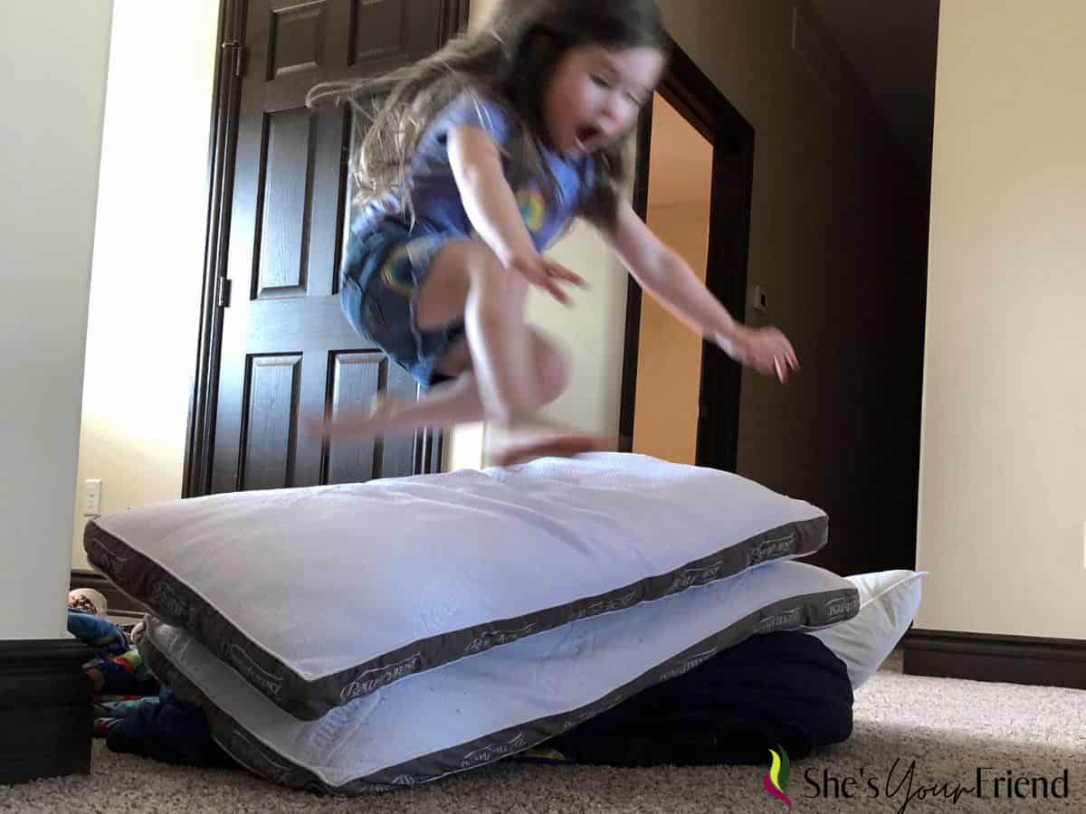 a girl jumping over a stack of pillows.