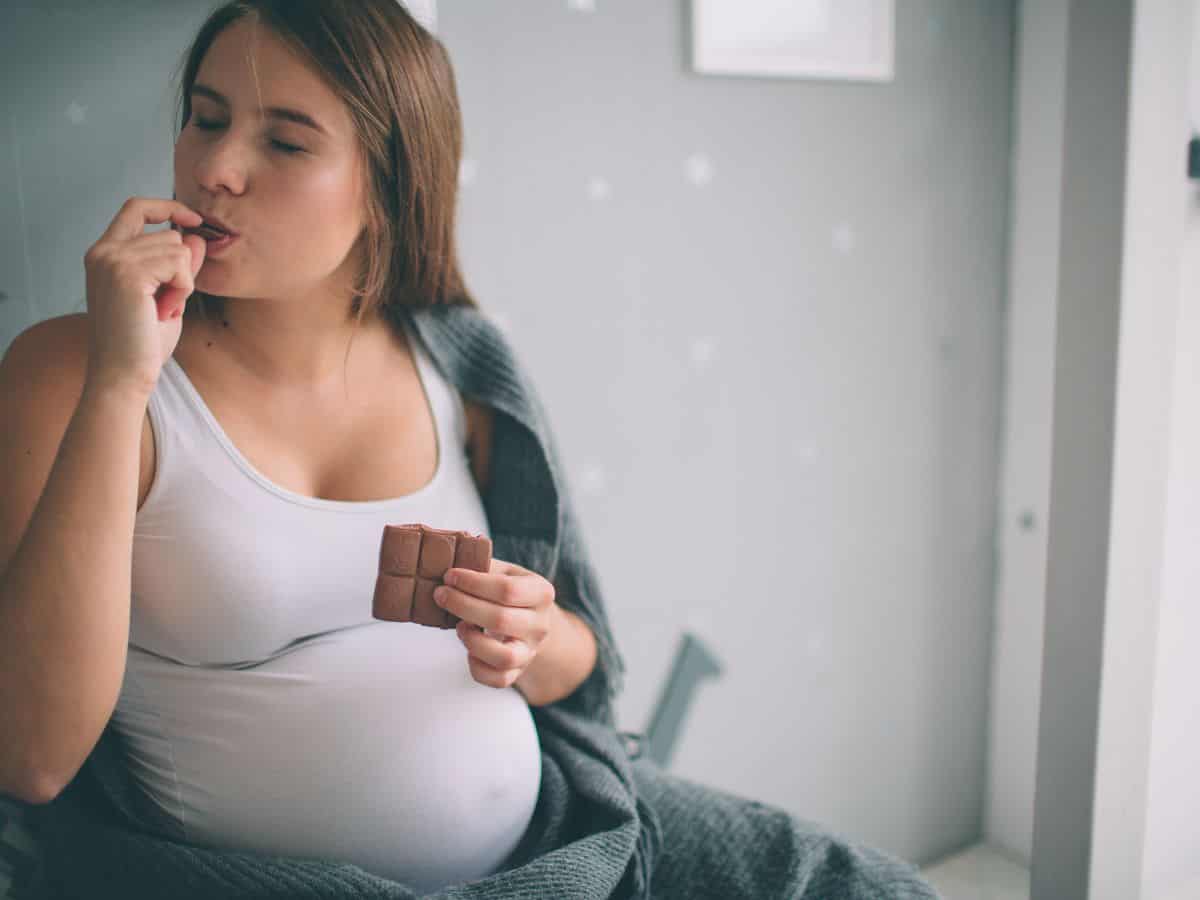 a pregnant woman eating a piece of chocolate