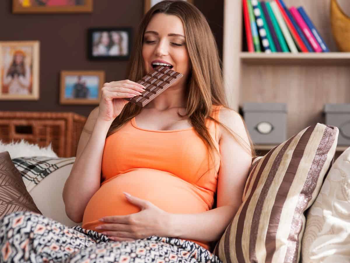 a pregnant woman sitting on a couch eating some chocolate