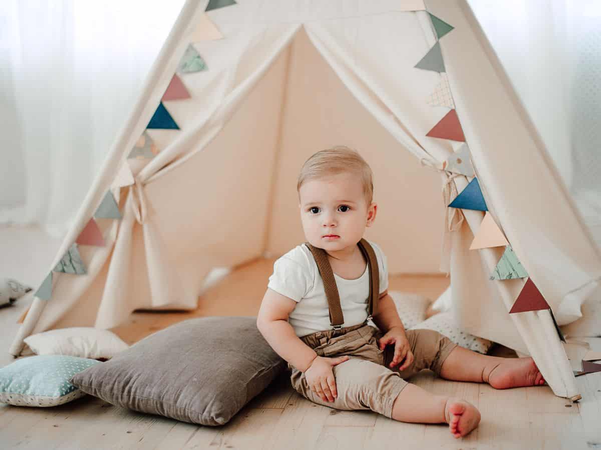 a baby boy sitting by a play tent and pillows