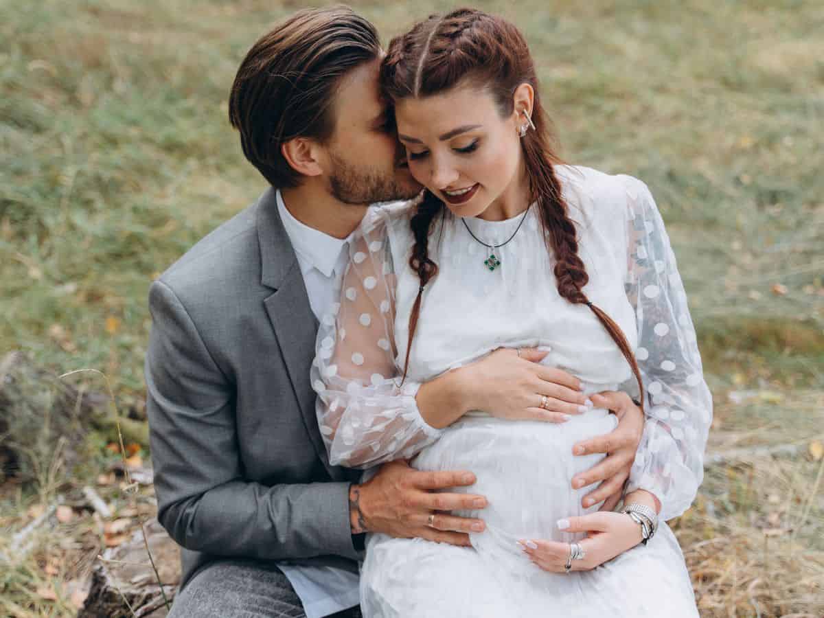 a pregnant woman wearing a wedding dress with her husband holding her