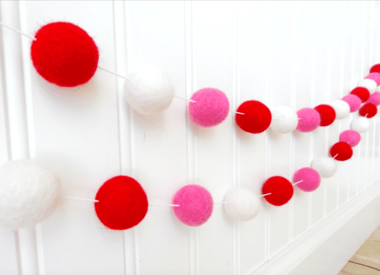 red pink and white felt ball garland hanging on a wall