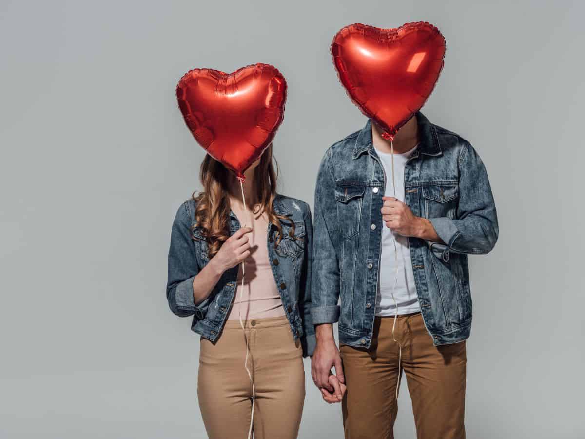 a couple holding hands and holding heart shaped balloons in front of their faces